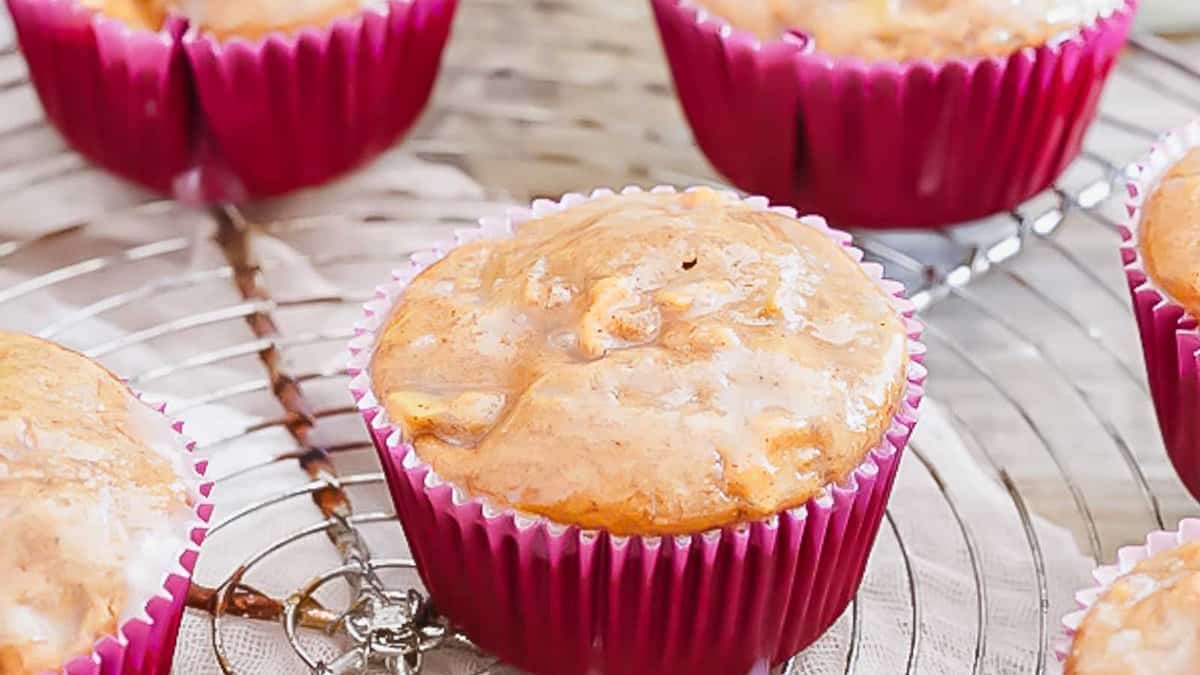 Four glazed muffins in pink paper liners are cooling on a metal wire rack.
