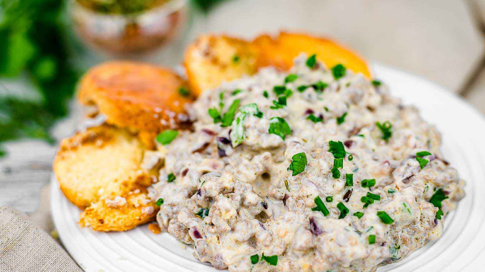 A plate of creamy sausage dip garnished with chopped chives, served with toasted bread slices on the side.