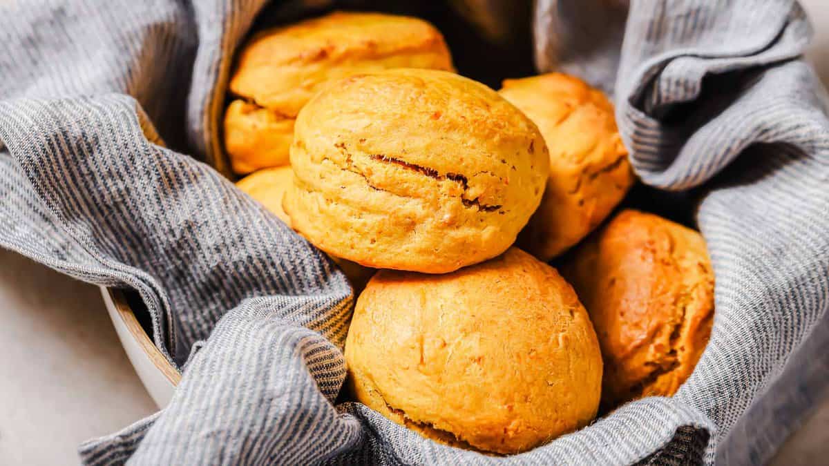 A bowl lined with a gray striped cloth holds several golden brown baked scones.