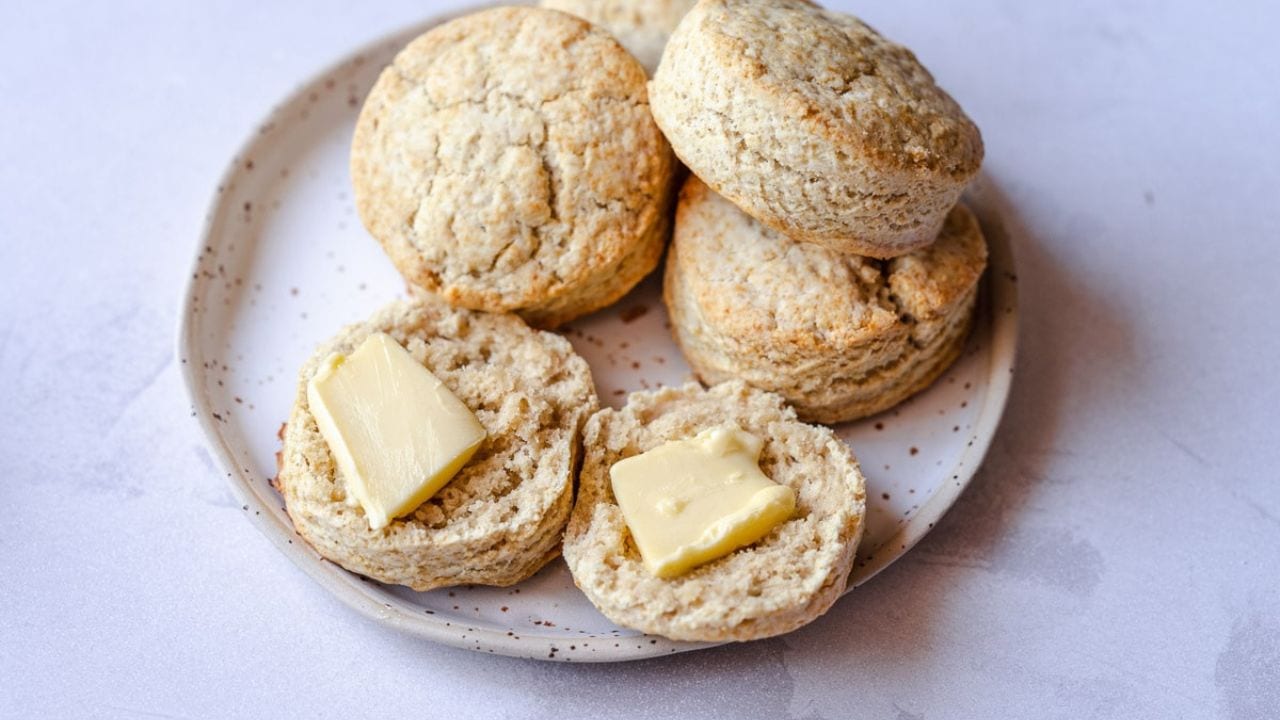 A plate with several baked biscuits, two of which are split open and topped with slices of butter.