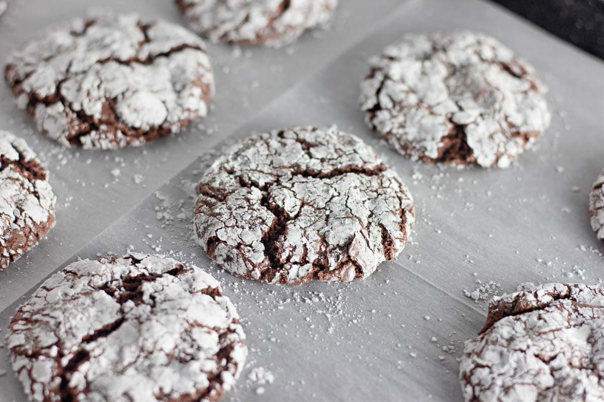 Chocolate crinkle cookies with powdered sugar on top, arranged on parchment paper.