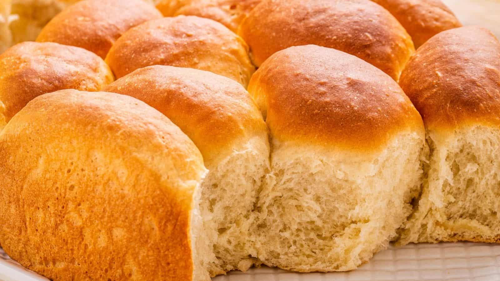 A close-up view of several golden brown, fluffy bread rolls arranged closely together on a white plate.