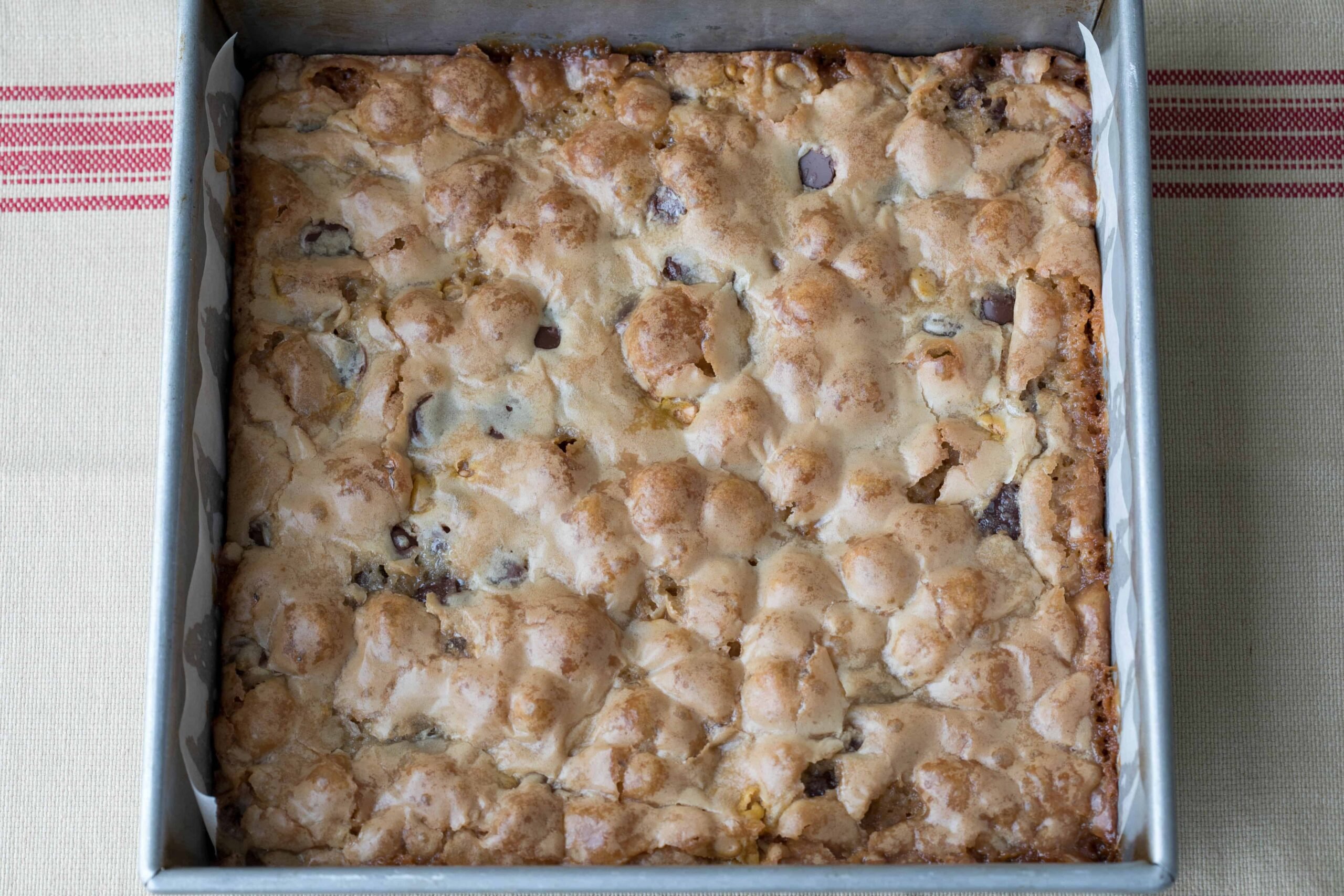 A square baking pan filled with baked dessert bars featuring a golden-brown, slightly cracked, and textured top.