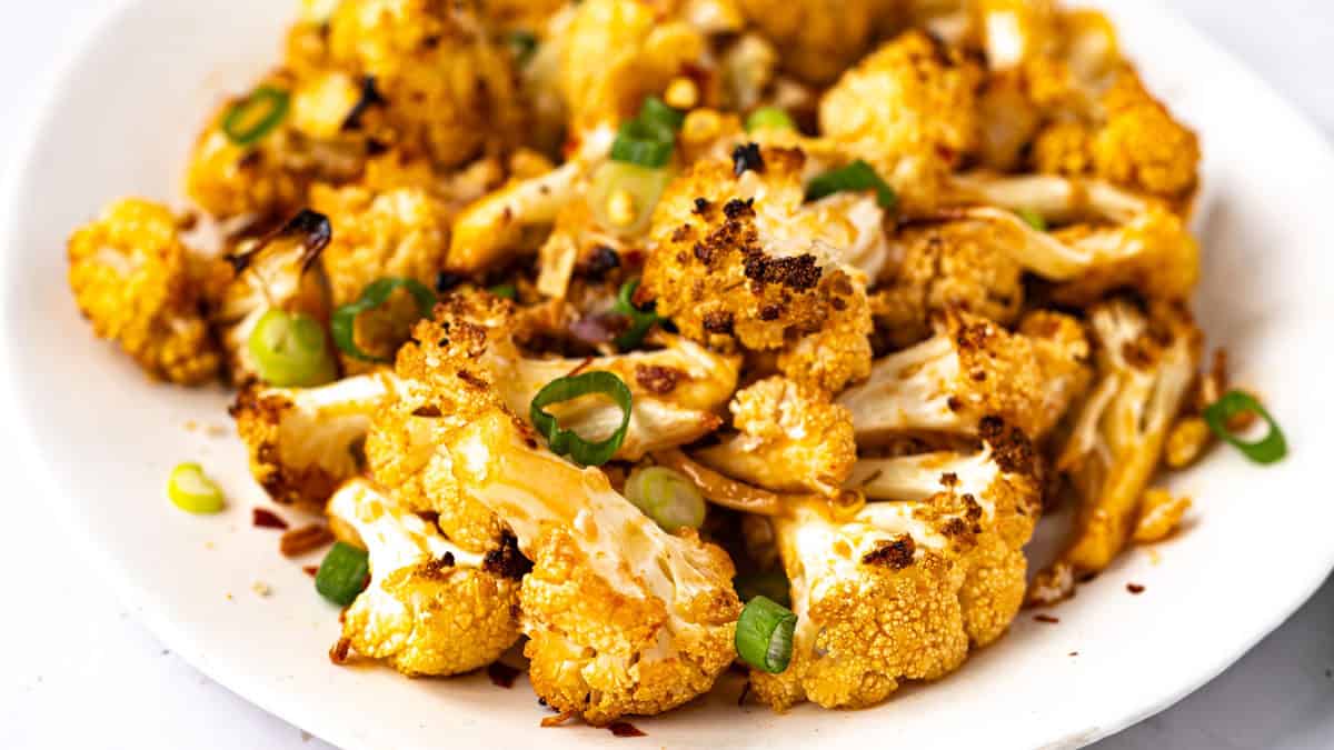 A plate of roasted cauliflower florets garnished with chopped green onions and red pepper flakes.