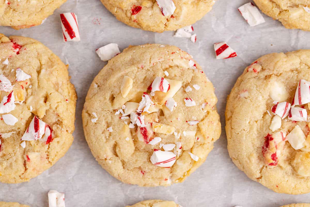 Close-up of cookies with pieces of crushed peppermint candy on top, arranged on parchment paper.