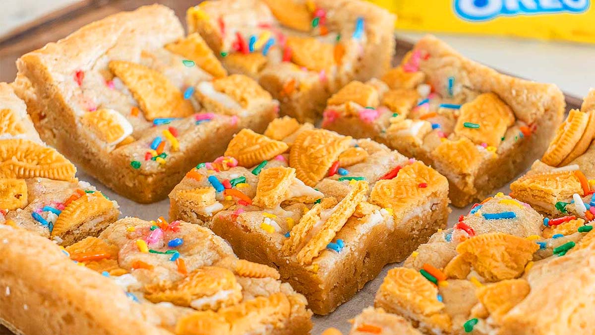 Cookie bars topped with broken golden cookies and colorful sprinkles, cut into squares and arranged on a baking tray.