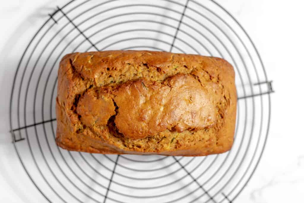 A loaf of bread cooling on a round wire rack, viewed from above on a white surface.