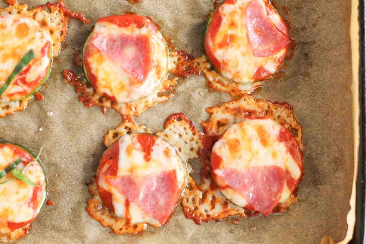 Mini pizzas with melted cheese and slices of pepperoni are baked on parchment paper in a sheet pan.