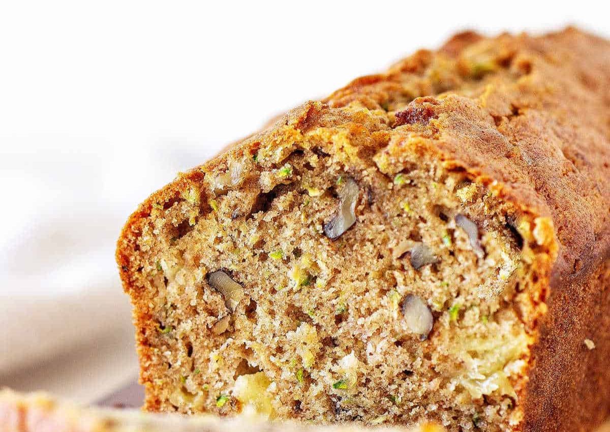 Close-up of a sliced loaf of zucchini bread with visible walnuts and a golden-brown crust.