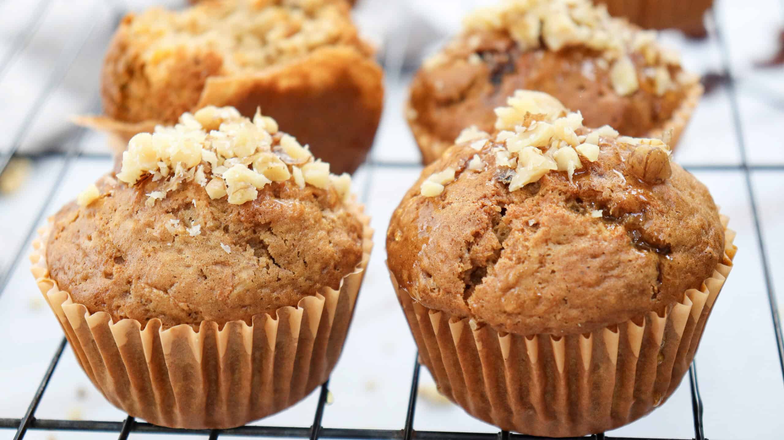 Four baked muffins with chopped nuts on top are placed on a cooling rack.
