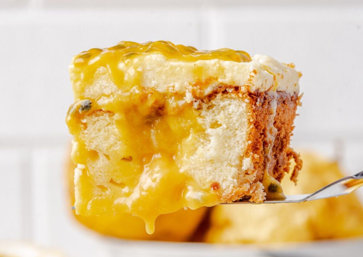 A close-up of a fork holding a slice of cake topped with a thick layer of yellow passionfruit sauce and frosting.