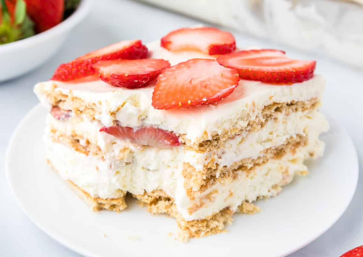 A slice of strawberry icebox cake with layers of whipped cream, graham crackers, and sliced strawberries on a white plate.