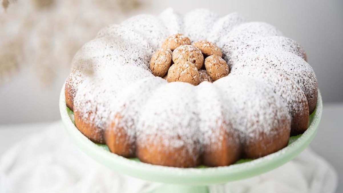 A bundt cake topped with powdered sugar and round cookies, displayed on a pale green cake stand.