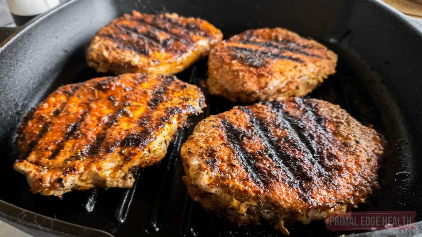 Four seasoned burger patties with grill marks are cooking in a black grill pan.