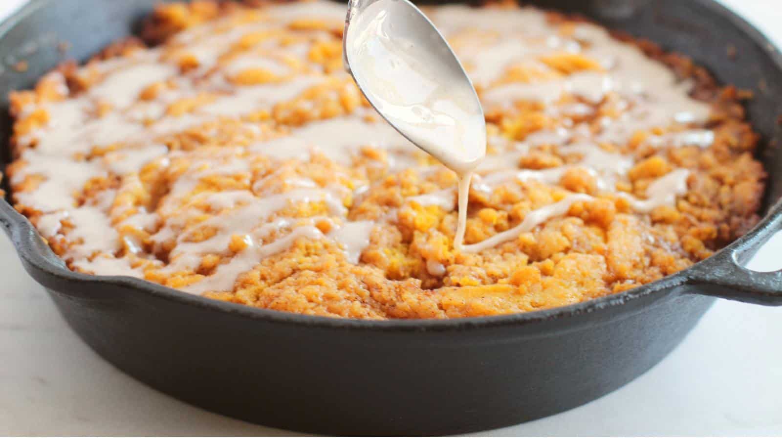 A spoon drizzles icing over a baked dessert in a black cast iron skillet.