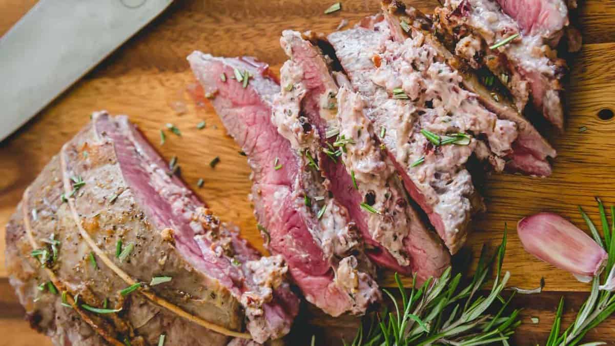 Sliced medium-rare beef roast topped with a creamy herb sauce, served on a wooden cutting board with fresh rosemary and garlic.