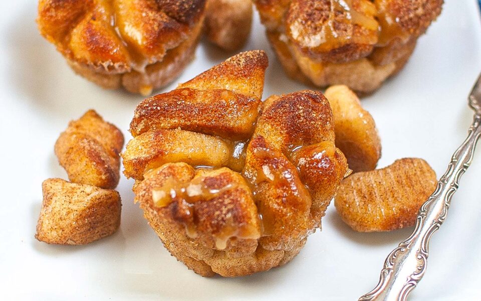 Mini monkey bread muffins coated in cinnamon sugar and drizzled with glaze, served on a white plate with a few pieces of dough on the side.