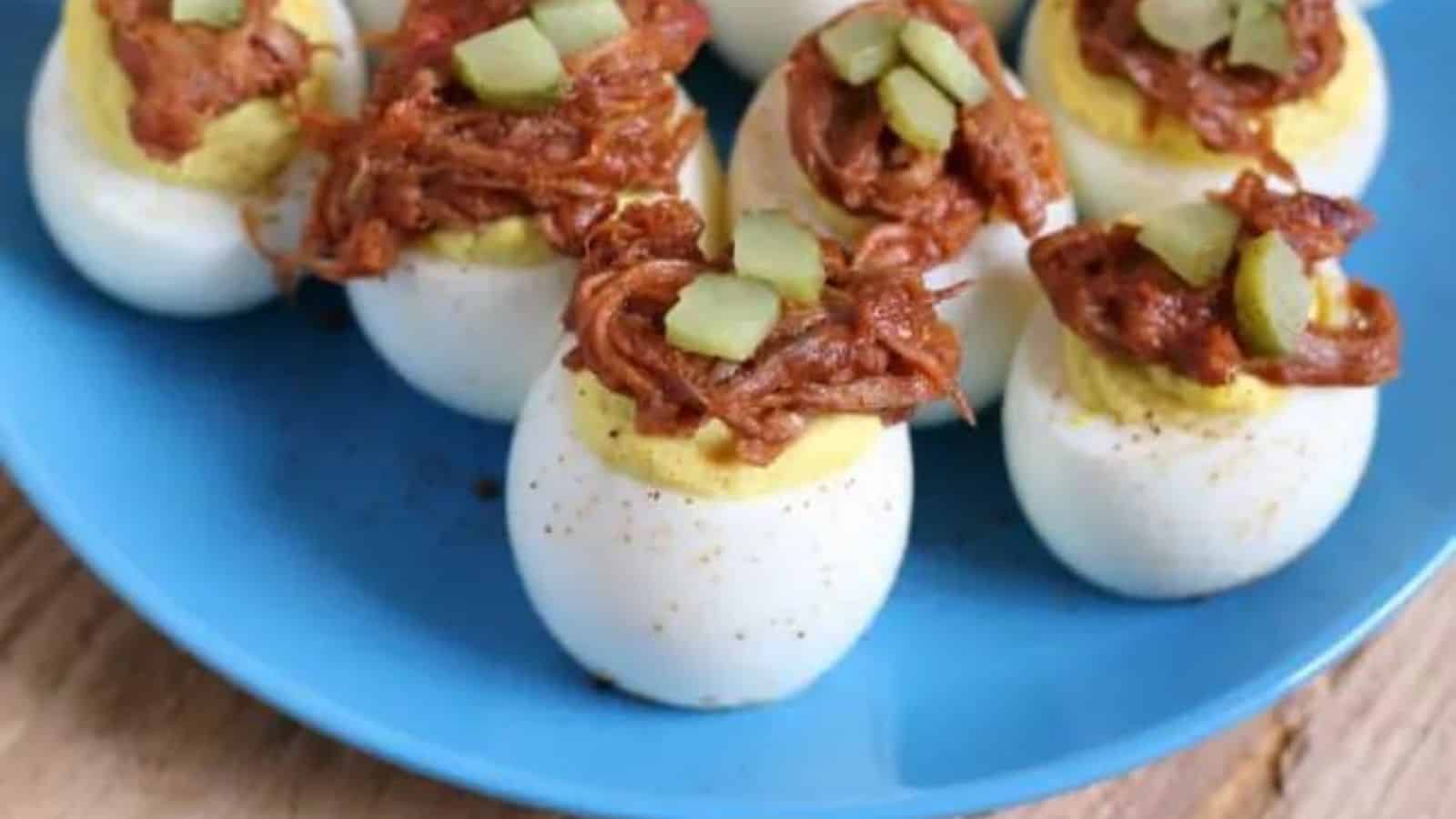 A blue plate with several hard-boiled eggs topped with shredded meat and small pieces of pickles.