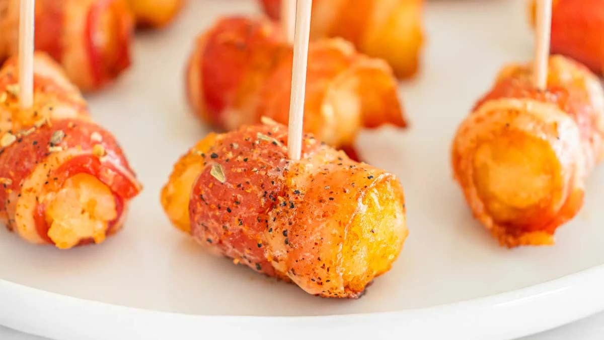 A close-up of bacon-wrapped tater tots secured with toothpicks, served on a white plate.