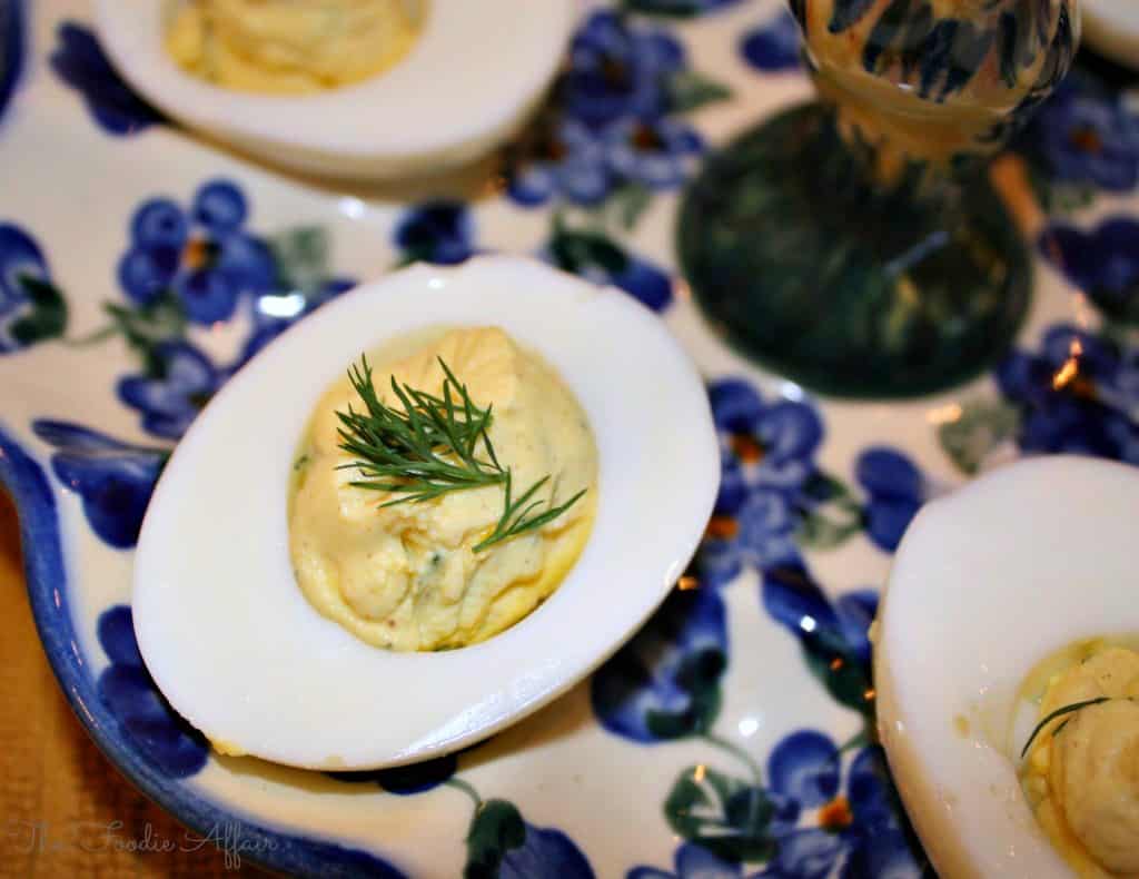 A deviled egg garnished with a sprig of dill is served on a floral-patterned plate.