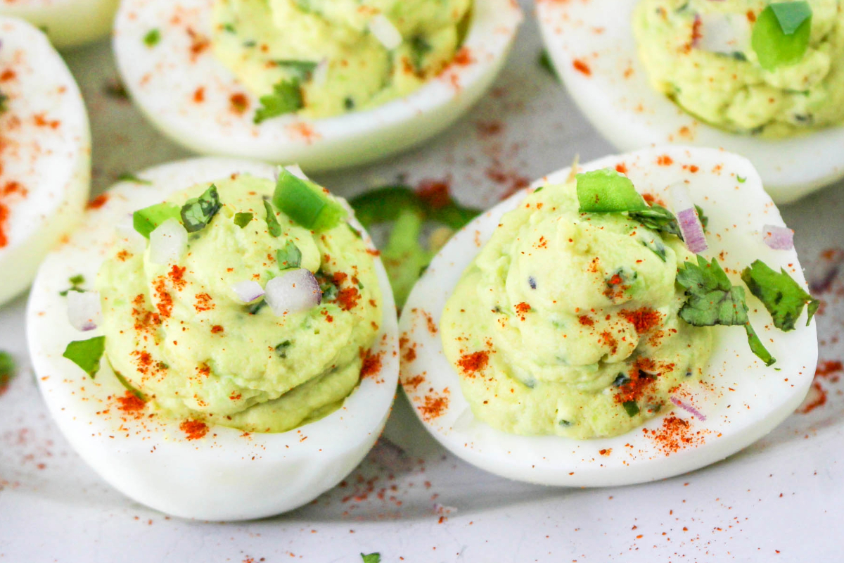 Close-up of deviled eggs filled with a creamy green mixture, topped with chopped herbs, onions, and a dusting of red paprika.