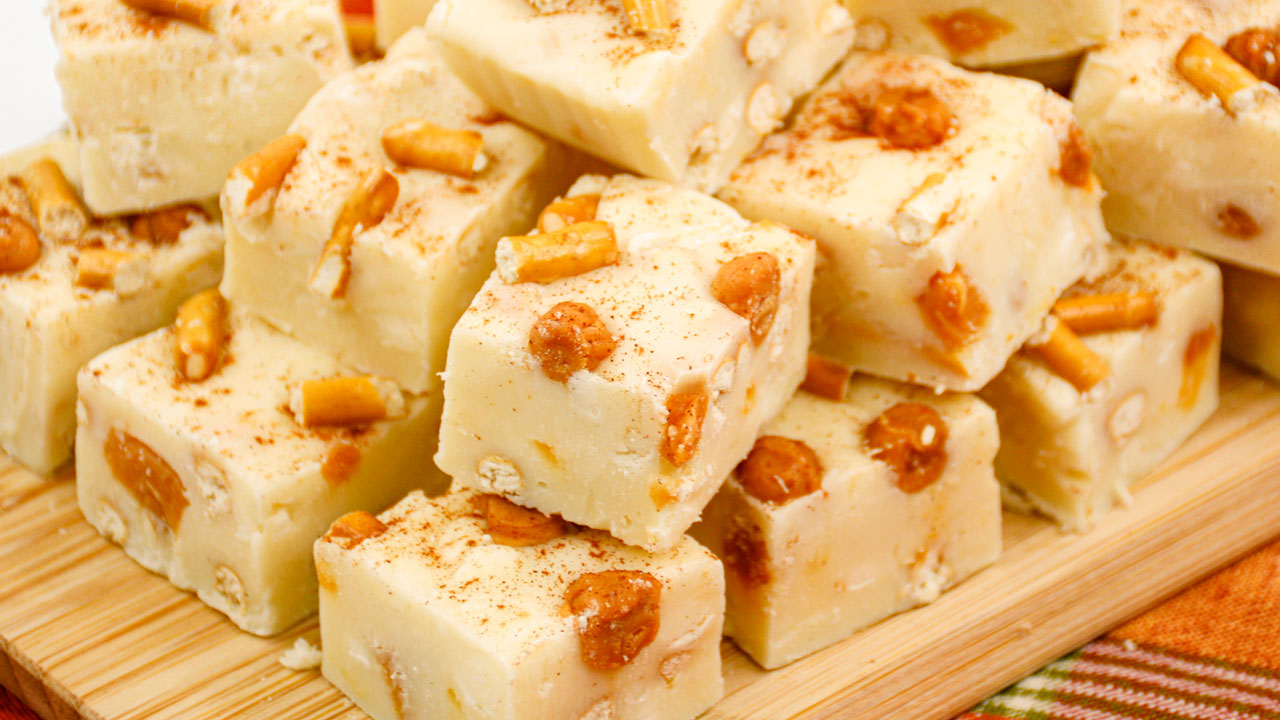 A stack of white fudge squares with pretzel pieces and caramel bits on a wooden tray.