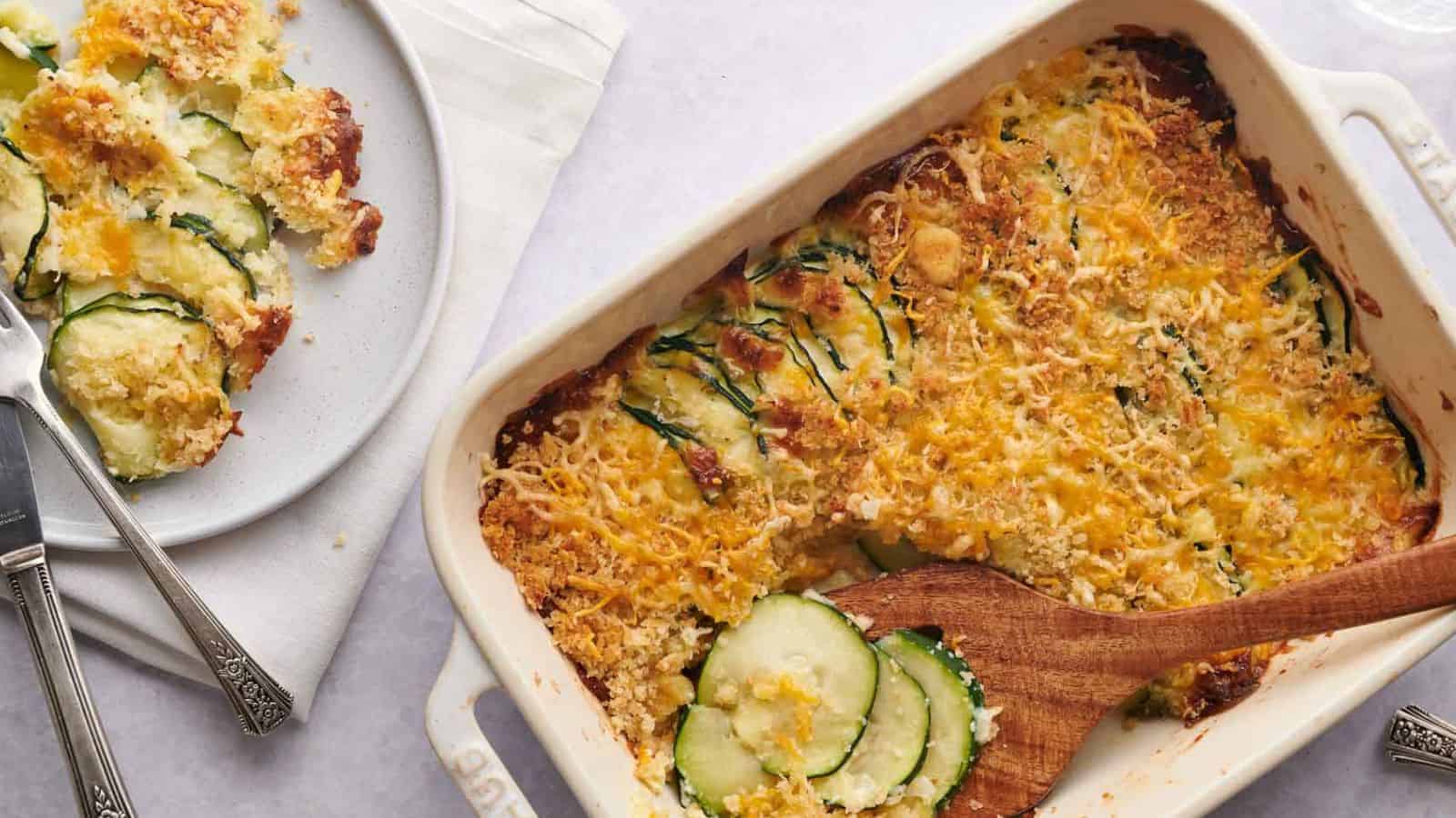 A baked casserole with sliced zucchini, cheese, and breadcrumbs is being served from a white dish onto a plate.