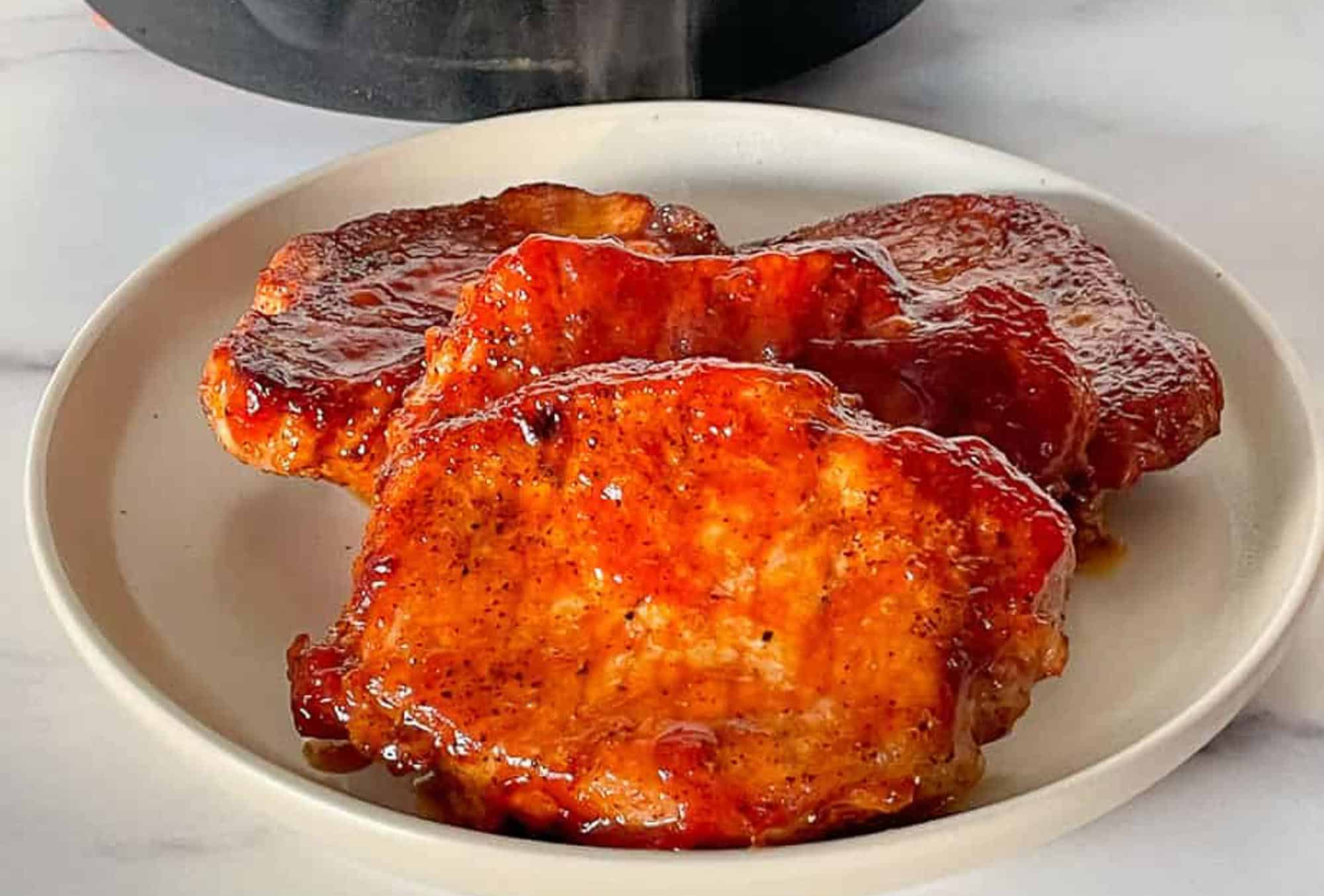 Three glazed pork chops with a shiny, reddish-brown sauce are arranged on a white plate.