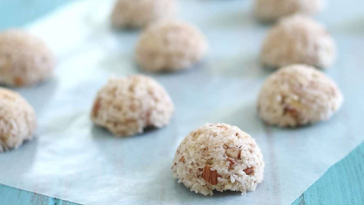 Eight coconut macaroons are arranged on a sheet of parchment paper atop a blue surface.