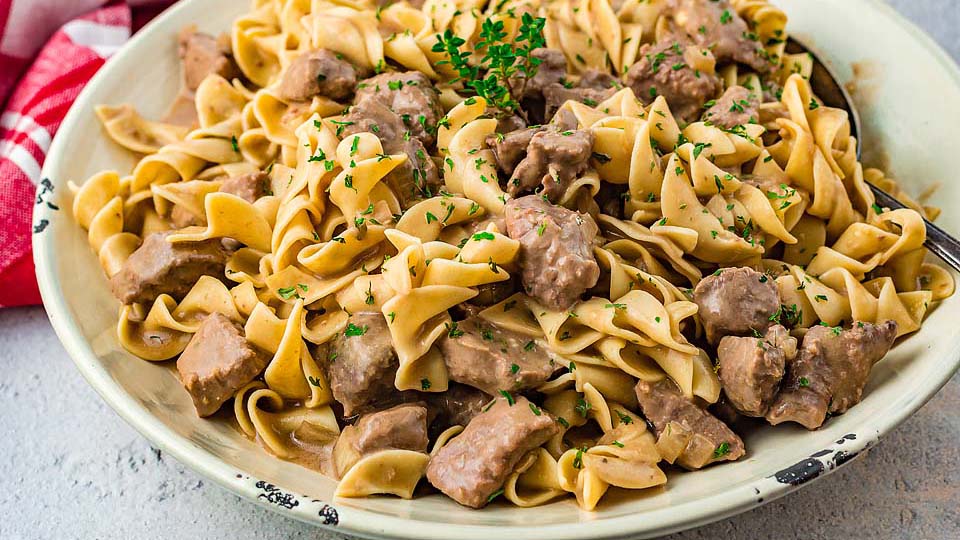A plate of beef stroganoff with egg noodles, garnished with chopped parsley.