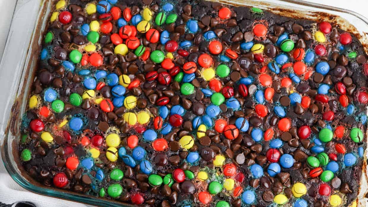 A glass baking dish filled with baked bars topped with colorful M&M candies and chocolate chips.