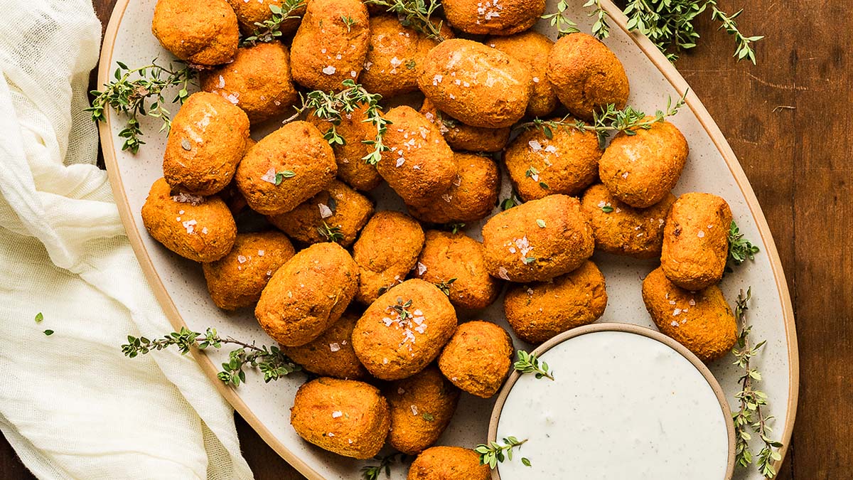 A platter of golden-brown, breaded nuggets garnished with herbs, served with a small bowl of creamy white dipping sauce.