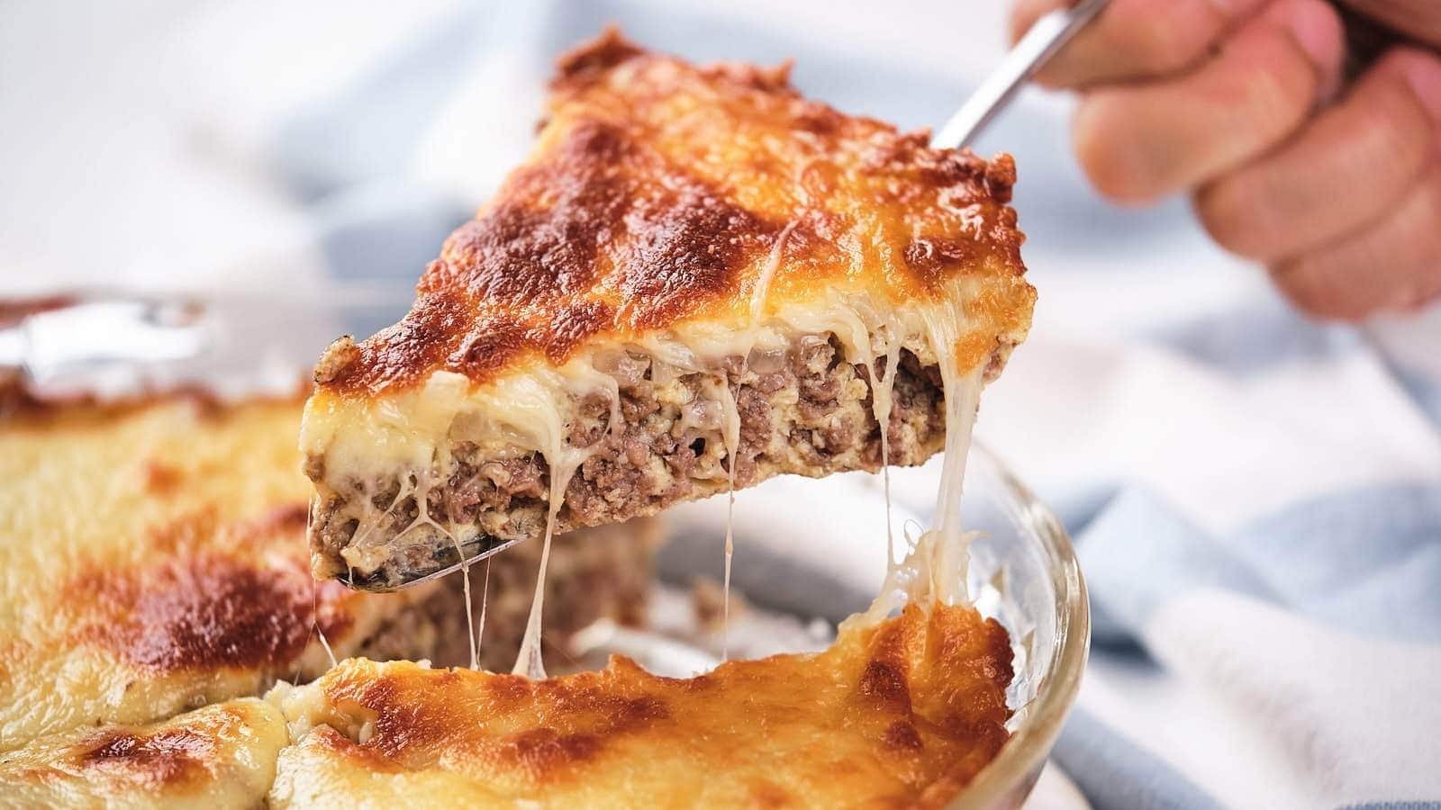 A slice of baked casserole with a browned, cheesy top and a ground meat filling being lifted from a glass dish.