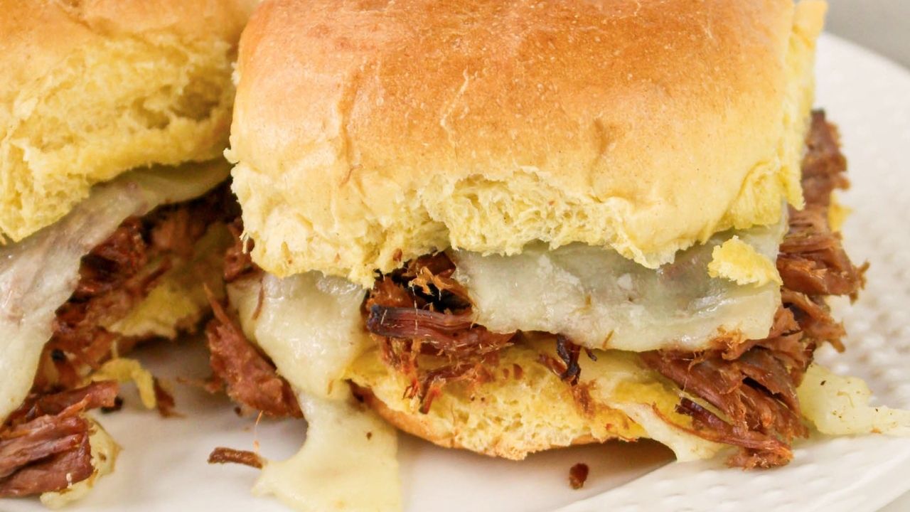 A close-up of a sandwich with shredded beef and melted cheese on a soft bun, placed on a white plate.