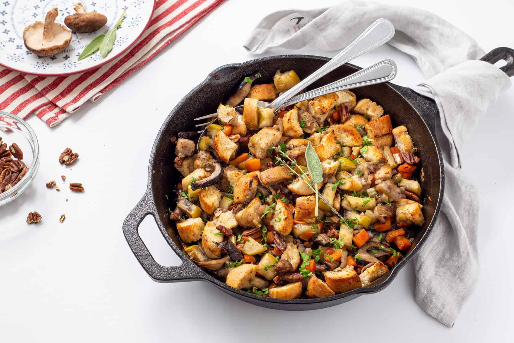A cast iron skillet filled with bread stuffing mixed with vegetables and herbs, with two forks resting inside.