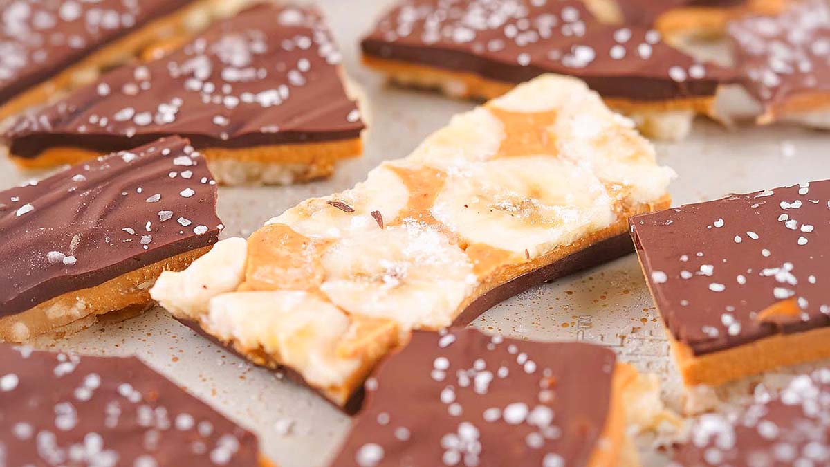 Pieces of chocolate-covered toffee bark with sea salt sprinkled on top are arranged on a flat surface.