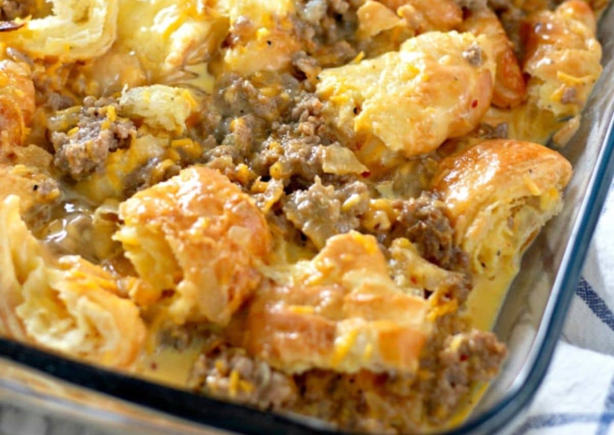 A glass baking dish filled with a baked casserole featuring ground sausage, melted cheese, and golden-brown, flaky biscuit pieces.