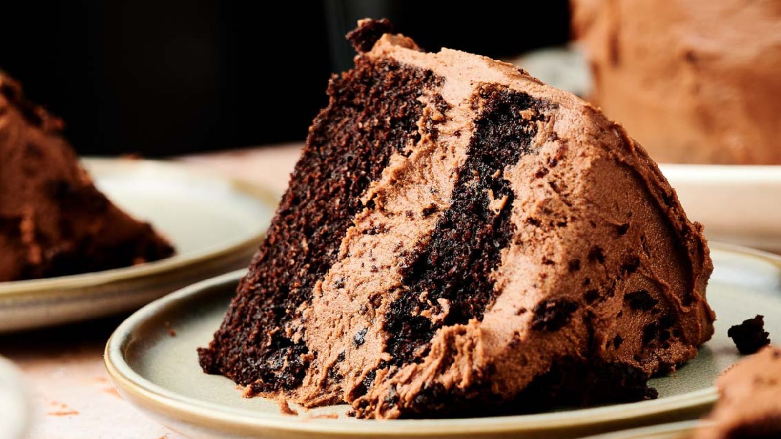 A slice of chocolate layer cake with chocolate frosting on a beige plate.