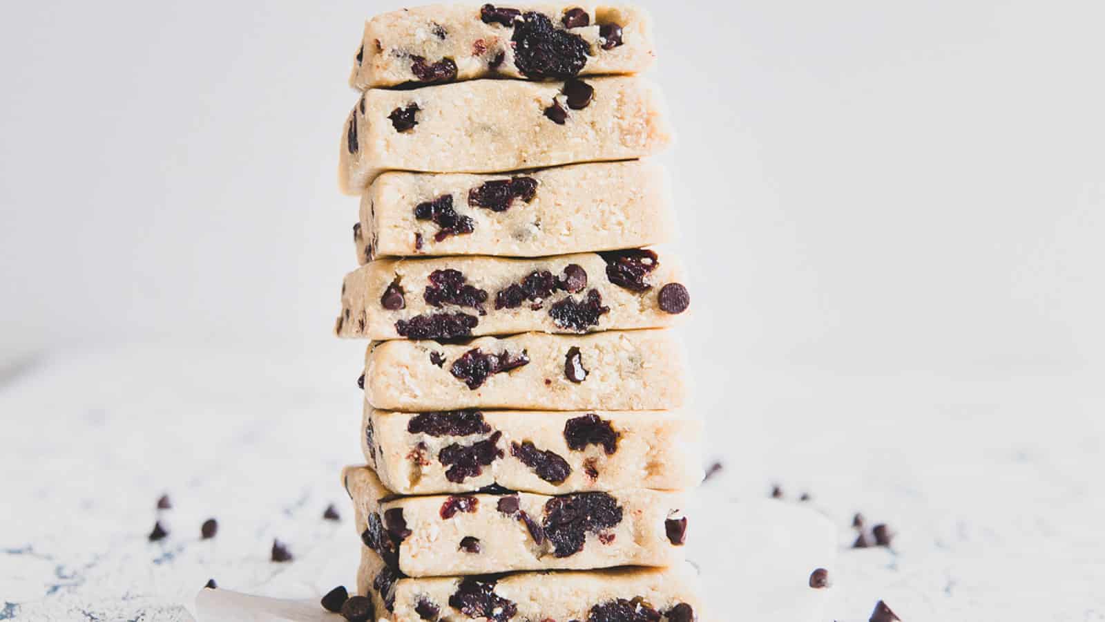 A stack of square shortbread cookies with chocolate chips, placed on a light surface with a few chocolate chips scattered around.