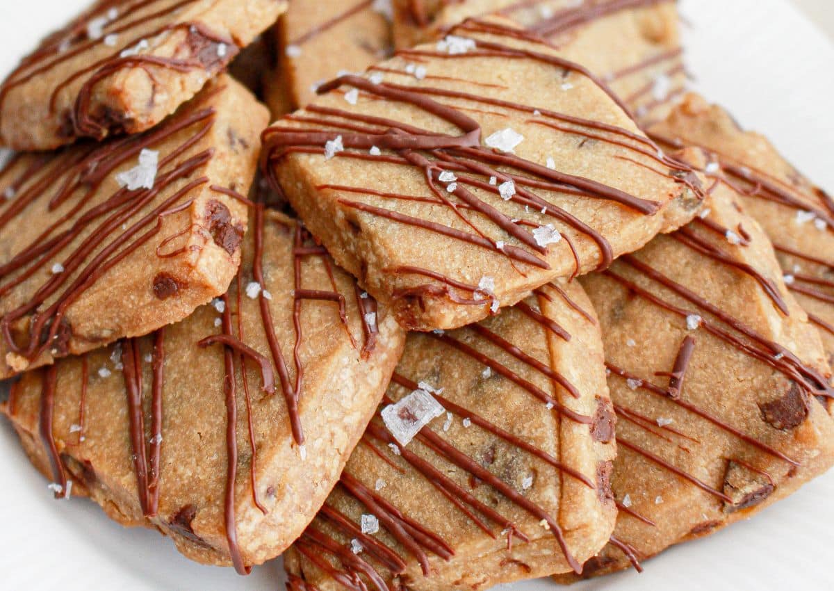 A plate of rectangular chocolate chip cookies drizzled with chocolate and sprinkled with coarse sea salt.