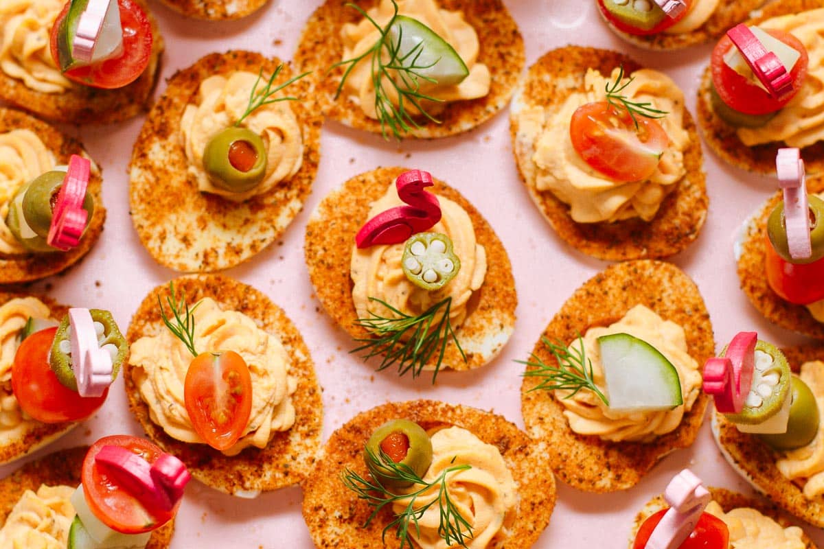 A tray of seasoned potato chips topped with a creamy spread, sliced vegetables, olives, fresh dill, and pickled onion.