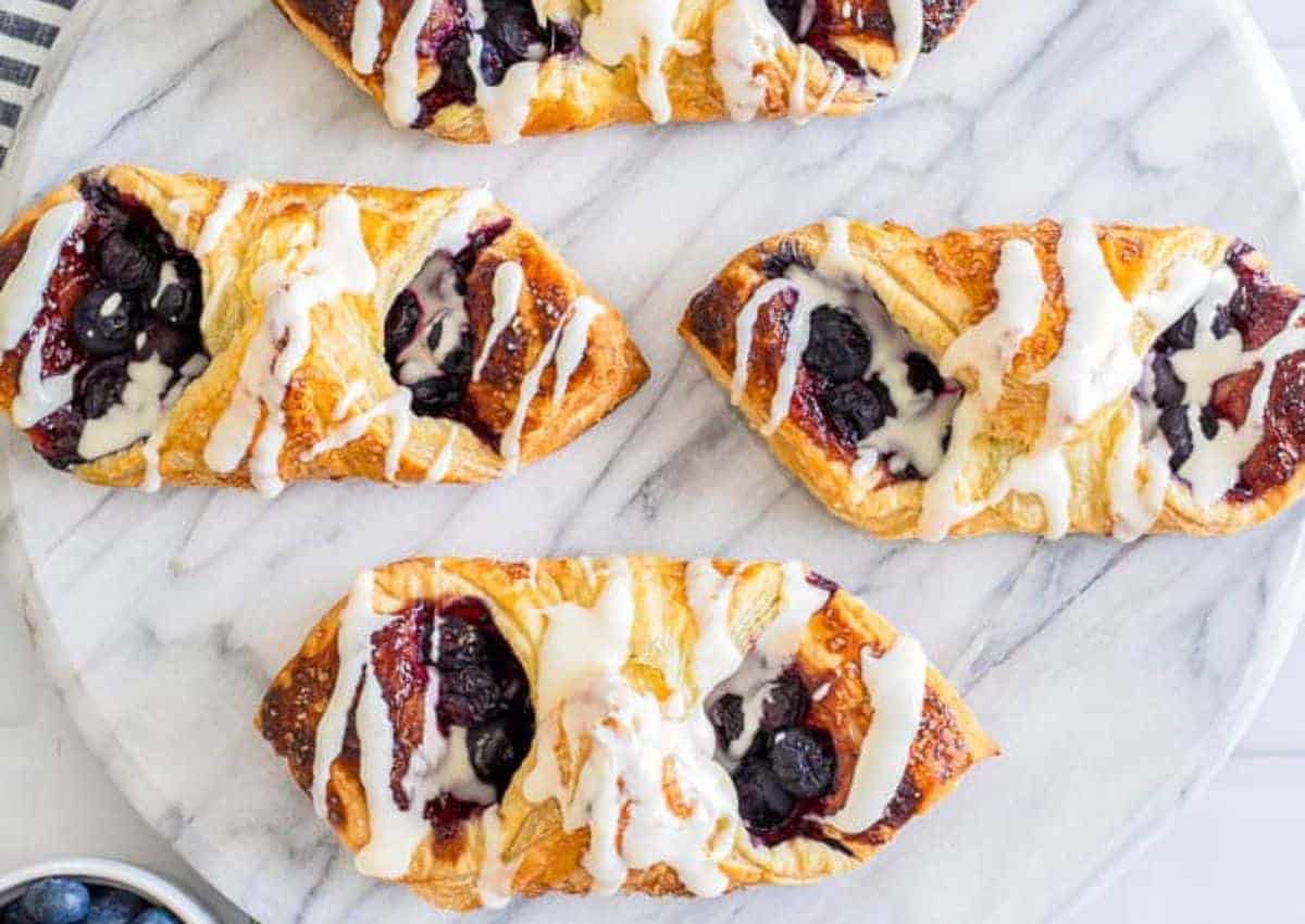 Four rectangular blueberry danishes with icing drizzle are arranged on a marble surface.
