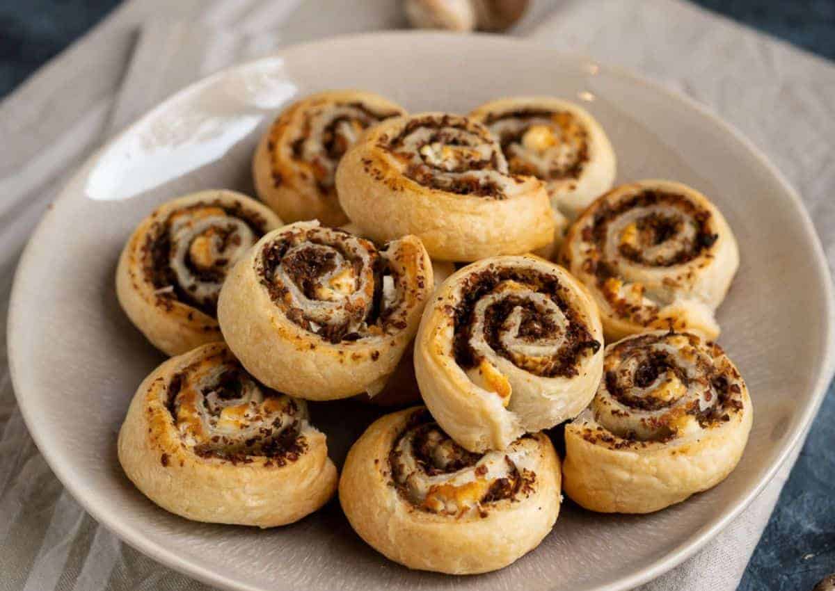 A plate of baked pinwheel pastries filled with a dark, likely savory filling, arranged in a circular pattern on a white dish.