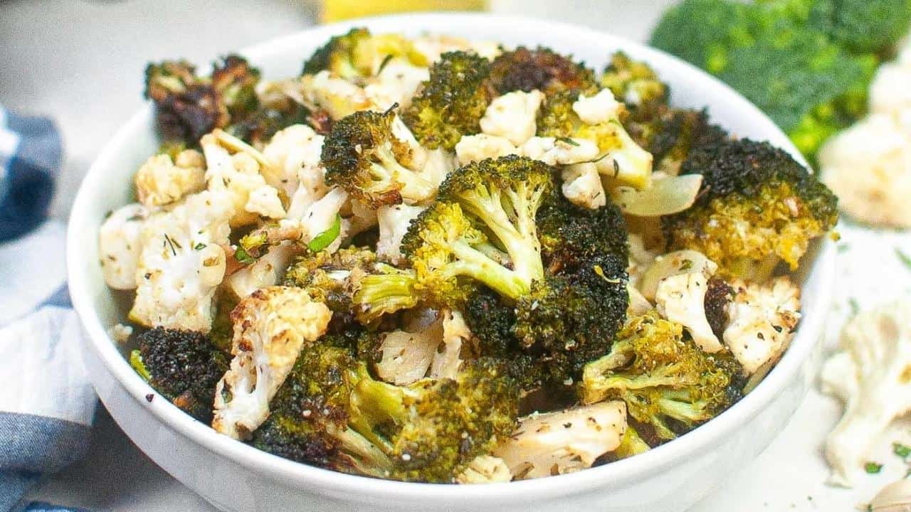 A white bowl filled with roasted broccoli and cauliflower florets, seasoned with herbs and spices.