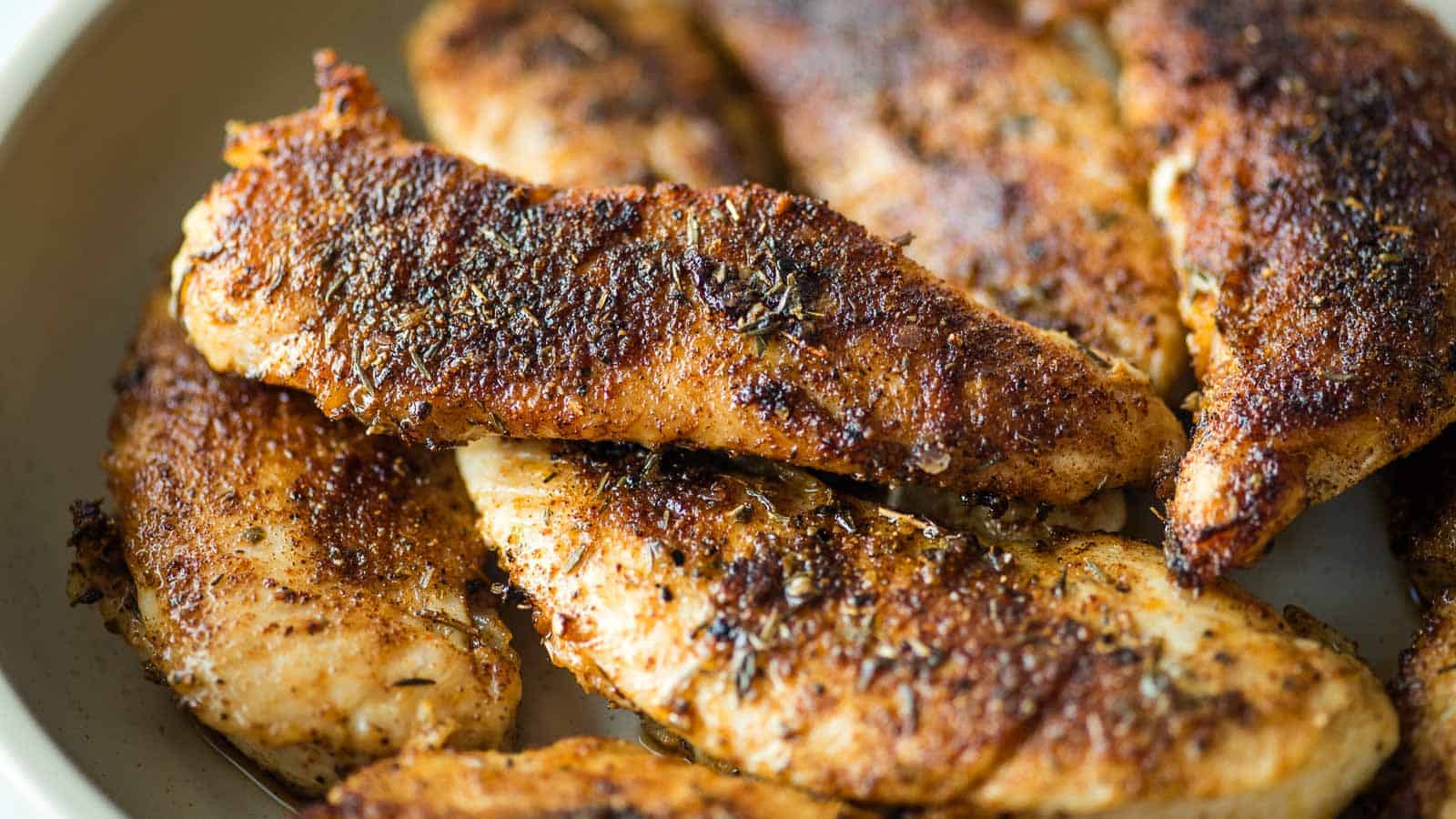 Several pieces of seasoned, cooked chicken breast are arranged in a shallow dish.