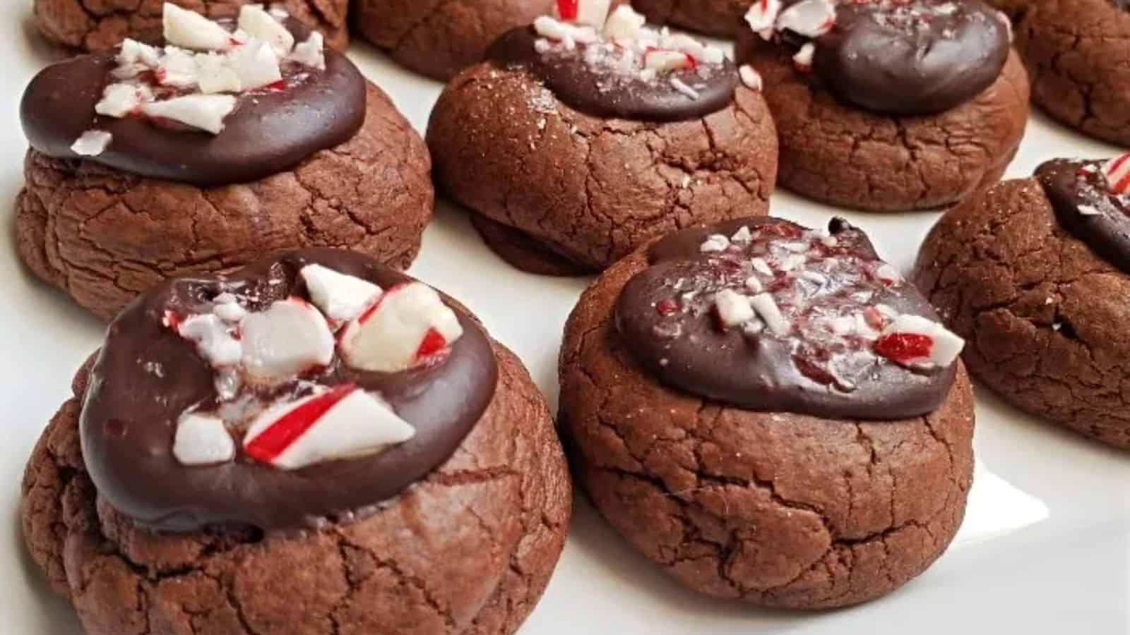 Chocolate cookies topped with a layer of chocolate and sprinkled with crushed peppermint candy, arranged on a white surface.