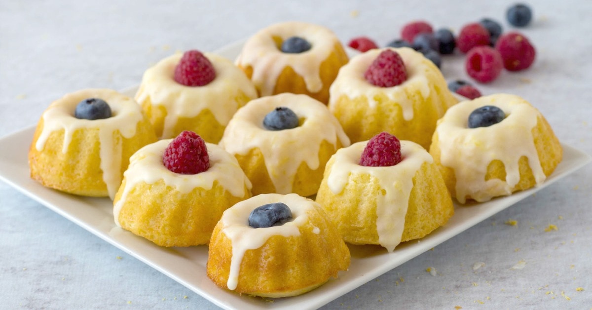 A plate of mini bundt cakes topped with white icing and garnished with fresh blueberries and raspberries.