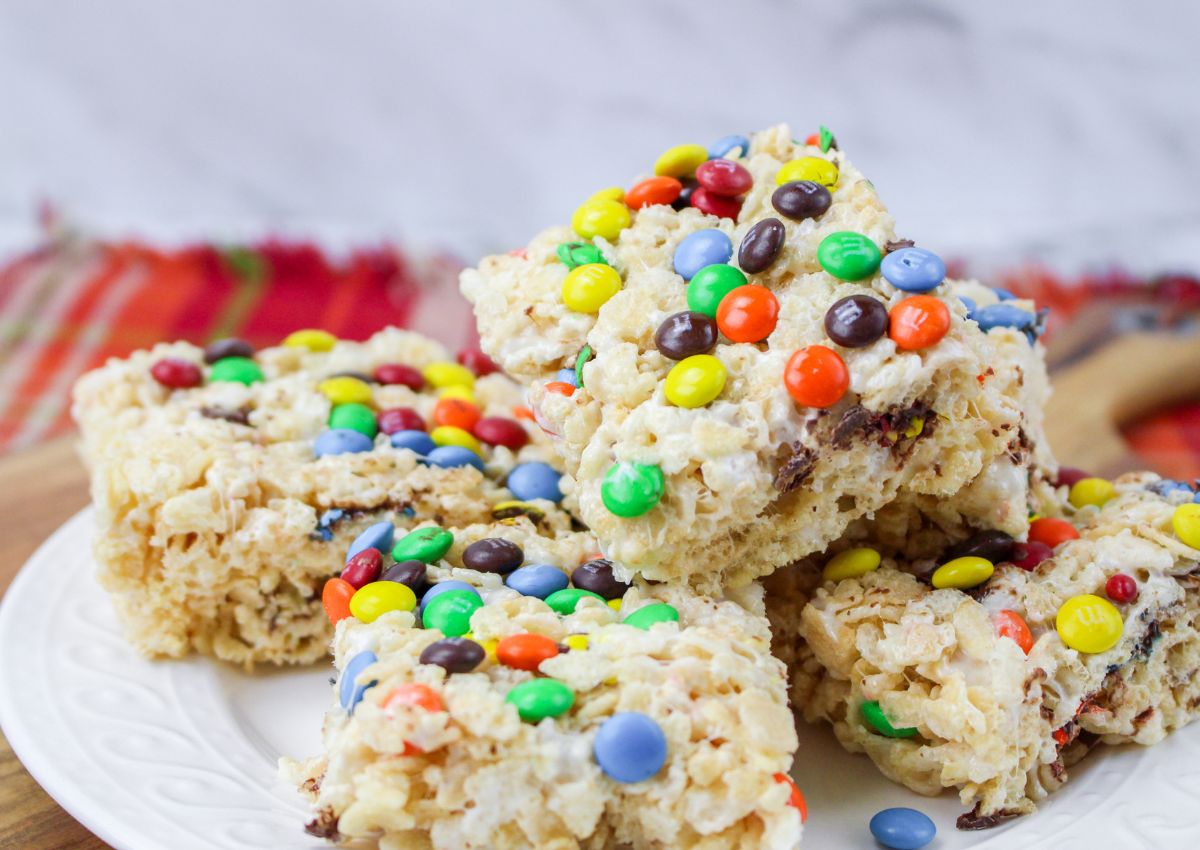 Rice Krispies treats topped with colorful candy-coated chocolates are stacked on a white plate.