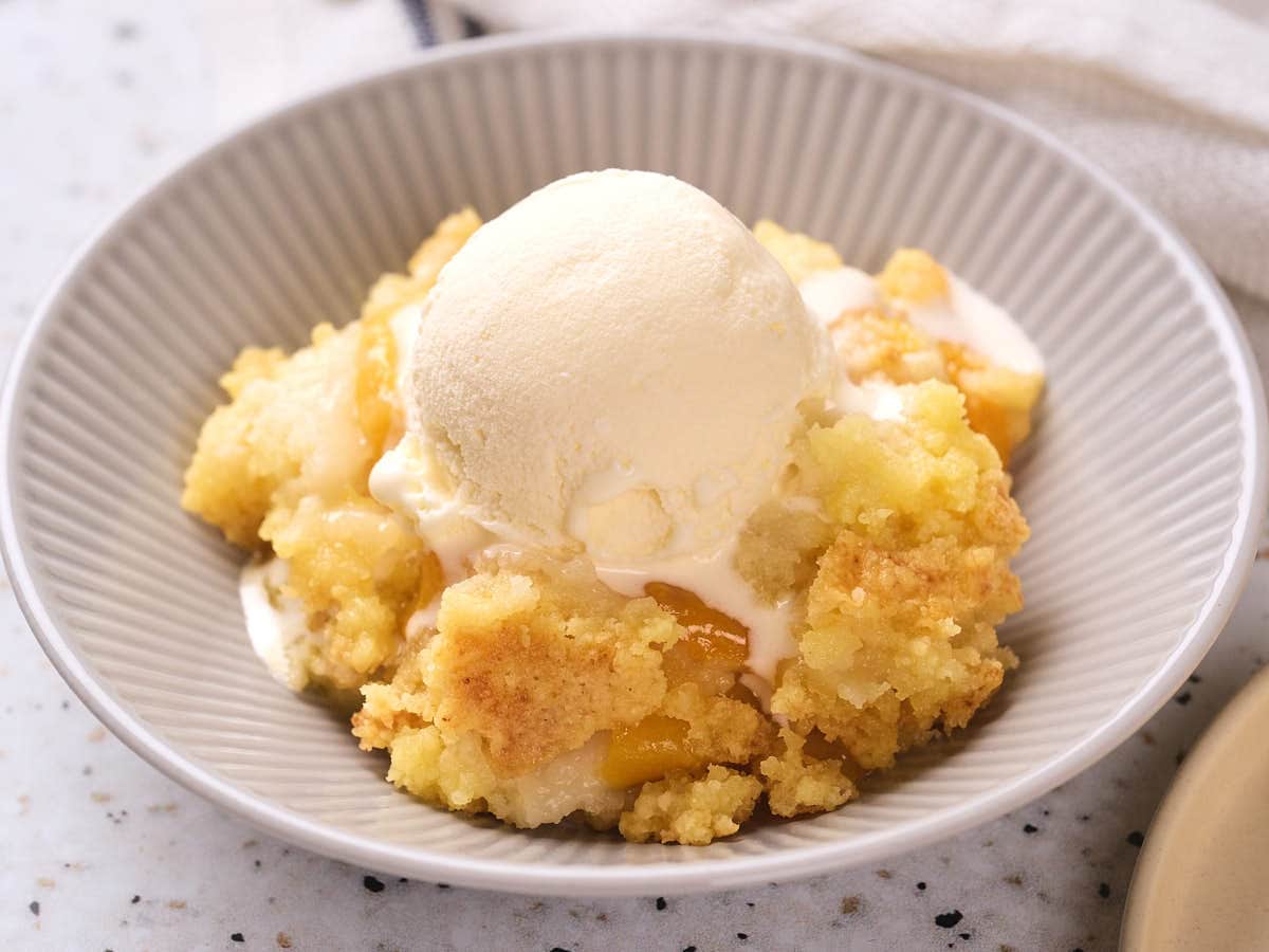 A bowl of peach cobbler topped with a scoop of vanilla ice cream.