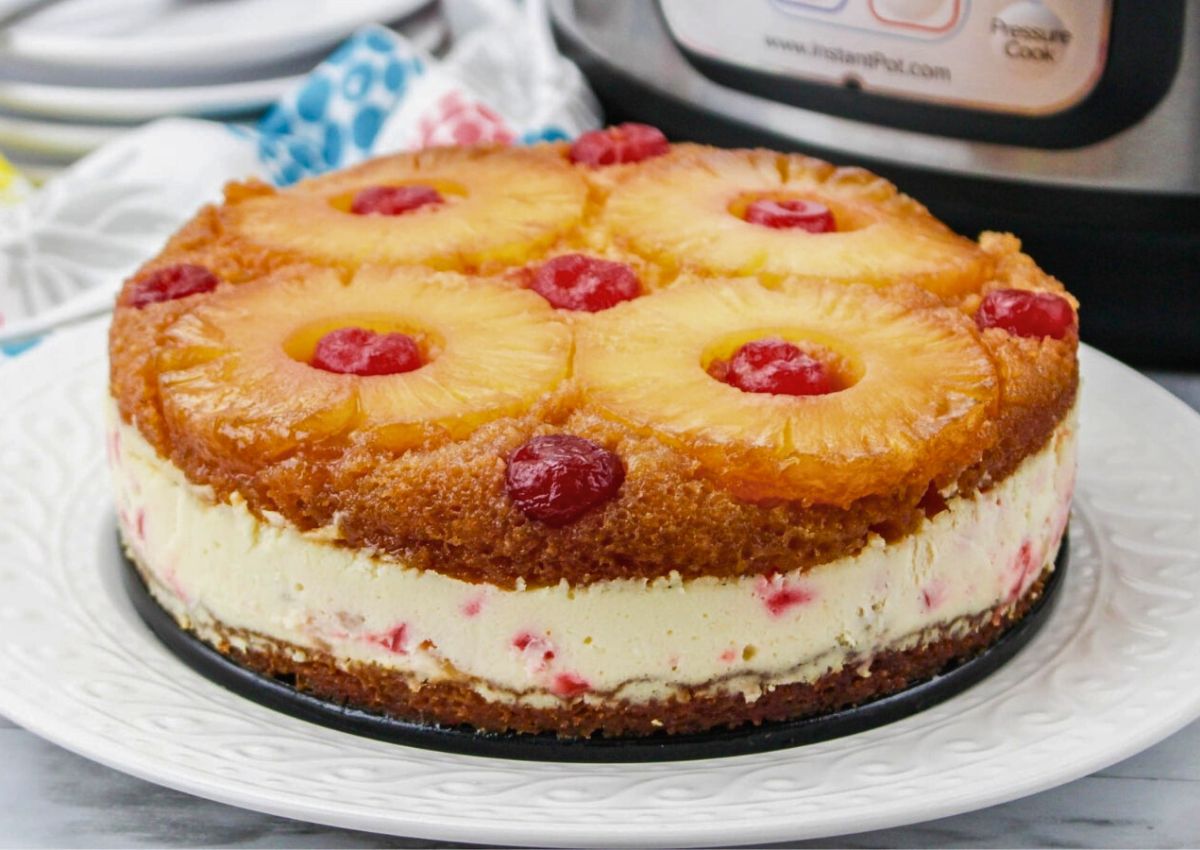 A pineapple upside-down cake with cherries on top, featuring a creamy layer in the middle, is displayed on a white plate.
